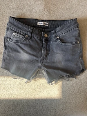 Grå jeansshorts Acne Jeans - Snygga grå jeansshorts från Acne Jeans med råa, fransiga kanter och klassisk femficksdesign. Shortsen har knapp och dragkedja framtill samt bälteshällor. Perfekta för en avslappnad stil under varma dagar.