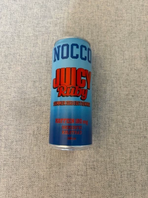 NOCCO Juicy Ruby Summer 2023 - NOCCO Juicy Ruby Summer 2023 Edition är en kolsyrad energidryck med koffein (180 mg), sockerfri och BCAA. Burken är blå med röd och blå text, rymmer 330 ml och var limeted edition 