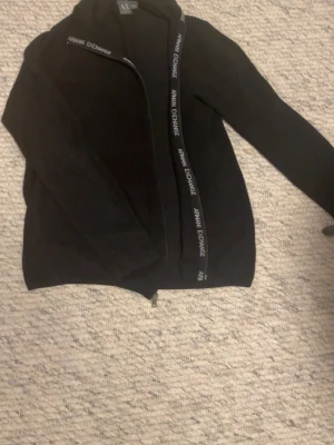 Svart ziptröja från Armani Exchange - Svart ribbstickad ziptröja från Armani Exchange , Nypris runt 1200 kr, med dragkedja och logotypdetaljer längs dragkedjan. Tröjan har  lång ärm och är perfekt för en stilren och modern look. Hör av dig med funderingar eller prisförslag 🤩