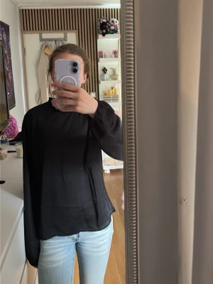 Svart långärmad blus - Säljer en svart blus med lång ärm och resår vid ärmsluten. Blusen har en rak passform och hög hals, vilket ger en stilren look. perfekt för att matcha med jeans eller kjol.❤️