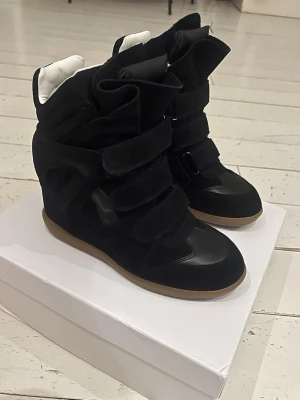 Wedge sneakers svarta - Bekett wedge sneakers i svart, nyskick!🌸Snygga svarta sneakers med inbyggdklack på 5cm, och flera kardborreband. Skorna har detaljer i mocka och läder, samt vit insida och brun sula. Pris kan diskuteras men föredrar fast pris. Begagnade av mig, men kommer ej till användning och endast använda inomhus. Verifiering visas i bild 6/7.