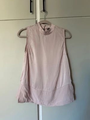 Ljusrosa ärmlös topp med slits - Snygg ljusrosa ärmlös topp med hög hals och slits i sidan. Fint skick! 