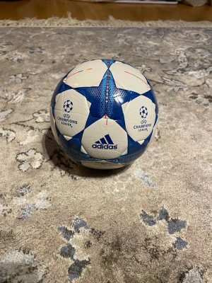 Adidas Champions League fotboll mini boll size 1 - Säljer en officiell Adidas Champions League fotboll i vitt och blått med stjärnmönster. Bollen har tryckt Champions League-logga och Adidas-logga. Perfekt för dig som älskar fotboll och vill ha en snygg boll att spela med eller samla på. !!!Behöver endast pumpas!!!