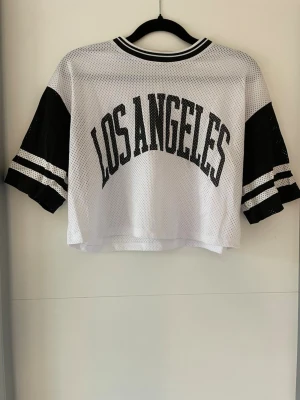 Vit och svart croppad topp - Sportig croppad mesh-topp i vitt med svarta ärmar och texten 'Los Angeles' i svart.