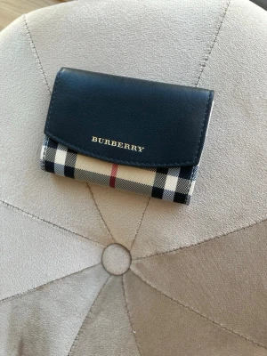 Burberry korthållare i svart och beige - Säljer min snygga korthållare/ lilla plånbok från Burberry med klassiskt rutmönster. Ovansidan är i svart läder med guldfärgad logotyp. Perfekt storlek för kort och några sedlar. Stilren och tidlös design. Utan egentliga tecken på användning och väldigt väl omhändertagen. Köpt direkt från butiken. Fler bilder och mer information kan ges. 