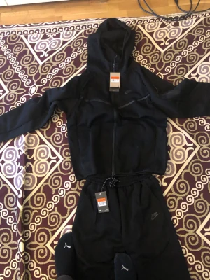 Nike tech tracksuit svart - Snygg svart Nike Tech Fleece hoodie med dragkedja och huva. Ikonisk design med diskret Nike-logga på bröstet och smarta detaljer som fickor med dragkedja. Perfekt för en sportig och stilren look. Materialet är mjukt och följsamt för extra komfort.