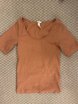 Ribbad brun topp med kort ärm - Snygg ribbad topp i brun färg med korta ärmar och rundad urringning. Perfekt att styla med jeans eller kjol för en trendig look. Materialet är mjukt och stretchigt för en bekväm passform.