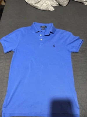 Blå pikétröja från Polo Ralph Lauren - Snygg blå pikétröja från Polo Ralph Lauren med klassisk krage och knäppning framtill. Tröjan har korta ärmar och den ikoniska broderade loggan på bröstet. Slim fit-modell som passar perfekt till jeans eller shorts. Storlek S. Jätte fin färg passar med linnebyxor och massa annat som jeans.