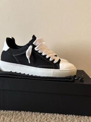 Svarta och vita sneakers från Numeris - Stilrena sneakers från Numeris i svart och vitt med breda vita skosnören och kontrastsömmar. Skorna har en chunky vit sula och detaljerad häl med Numeris-logga. Ovandelen är i mockaliknande material och tåpartiet i vitt läder. Använts ett par gånger men ser ut som nya