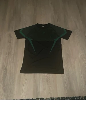 Röd och grön gymshark onyx - Två svarta Gymshark t-shirts med kort ärm och sportig passform. Ena har gröna detaljer och den andra röda, båda med Gymshark-logga på bröstet. Perfekta för träning eller gymmet, tillverkade i ett lätt och stretchigt material.