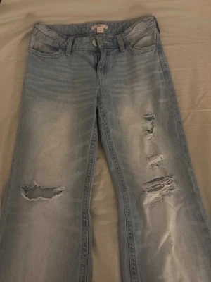 Ljusblå jeans me hål - Säljer ett par ljusblå jeans med slitningar och hål på benen. Jeansen har klassisk femficksdesign, bälteshällor och dragkedja med knapp. Perfekta för en avslappnad och trendig look. Jag är 162 och dom går ner till marken