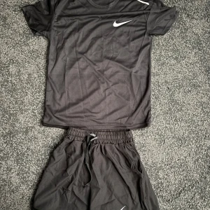 Svart nike Miller set  -  Nike Miller Svart t-shirt och shorts från Nike Miller i lätt och ventilerande funktionsmaterial. Klassisk rund halsringning, korta ärmar och vit Nike-logga på bröstet. Perfekt för träning och sportiga dagar. Är ganska tajt.
