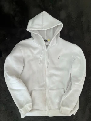 Vit hoodie från Polo Ralph Lauren - Säljer en clean vit hoodie från Polo Ralph Lauren. Tröjan har två fickor fram och den ikoniska lilla loggan broderad på bröstet. Perfekt för en avslappnad och stilren look. Tröjan har en liten fläck på baksidan men är inte märkvärdig, den är i storlek M varav pris går att diskutera