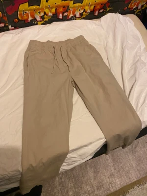 Beige linnes byxor  med dragsko - Säljer ett par beige mjukisbyxor med avslappnad passform och resår i midjan samt dragsko. Byxorna har två fickor bak och är perfekta för chill dagar. Materialet känns mjukt och skönt mot huden.