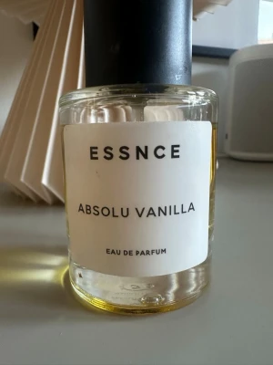 ESSNCE Absolu Vanilla Eau de Parfum - ESSNCE Absolu Vanilla Eau de Parfum med en stilren, rund glasflaska och svart lock. Parfymen har en varm gul vätska och en minimalistisk vit etikett med svart text. Doften har tydliga vaniljtoner och passar dig som gillar söta och mjuka parfymer. VILTIGT: Den är använd fåtal gånger 