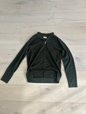 Mörkgrön halvzip tröja från Lindbergh  - Mörkgrön långärmad tröja med halv dragkedja i halsen. Tröjan har en klassisk passform och ribbade muddar vid ärmslut och nederkant. Perfekt för lager-på-lager och enkel att matcha med jeans eller chinos.