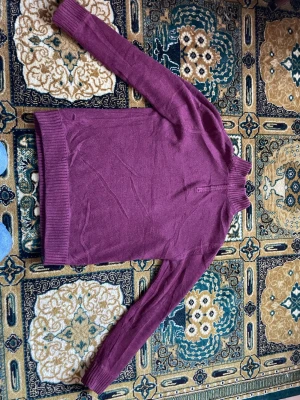 Vinröd halvzip-tröja från Eddie Bauer - Vinröd stickad tröja från Eddie Bauer med halv dragkedja och hög krage. Insidan av kragen är beige och ribbstickad. Perfekt för lager-på-lager och chill höststil.