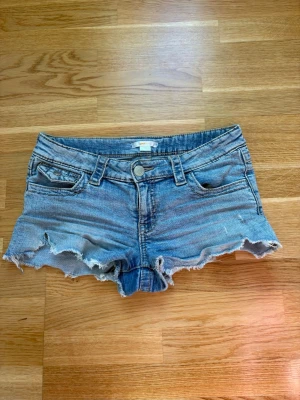 Blå jeansshorts med fransig kant - Snygga blå jeansshorts med fransig och rå kant nertill. Klassisk femficksmodell med knapp och dragkedja framtill samt bälteshällor. Perfekta för varma dagar och en avslappnad stil. Storlek 158 