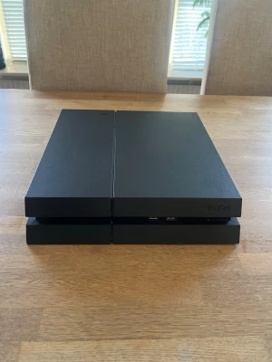 Sony PlayStation 4 svart konsol - Säljer en svart PlayStation 4 från Sony. Konsolen har en stilren, rektangulär design med mattsvart och glansig finish. Två USB-portar på framsidan och en tydlig ljuslist i mitten. Perfekt för gaming och streaming. 1 dosa följer med som funkar felfritt dock så är något löst innuti men den funkar som den ska! Har ingen laddare kvar då den gick sönder precis.  Alla spel ser ni på sista bilden