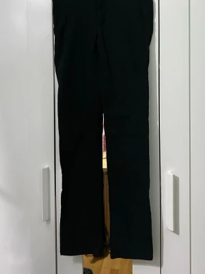 Svarta raka byxor - Svarta byxor med rak passform och klassisk design. Byxorna har en enkel look utan synliga detaljer eller mönster, vilket gör dem lätta att matcha med olika stilar. Perfekta för dig som gillar stilrena och minimalistiska plagg.