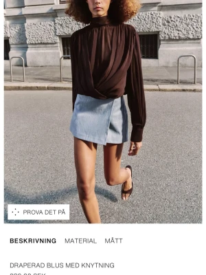 SÖKER!!!Brun draperad blus med knytning - Trendig brun blus med draperad front och knytning i midjan. Hög hals och långa ärmar ger en elegant siluett. Perfekt att styla med kjol eller jeans för en cool look.