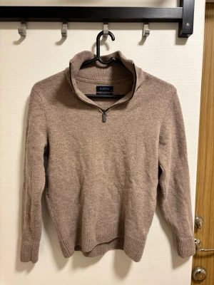 Beige stickad tröja med halv dragkedja - Stickad tröja från Dustin i beige nyans med halv dragkedja och hög krage. Tröjan har långa ärmar, ribbstickade muddar och nederkant. Perfekt för lager på lager och en avslappnad stil.