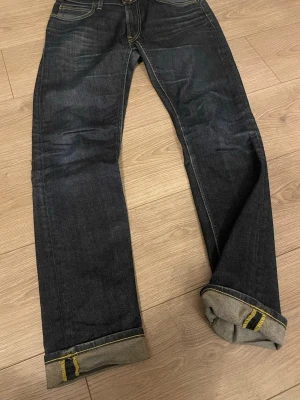Mörkblå jeans från Lee - Säljer folda ett par mörkblå jeans från Lee med klassisk femficksdesign och raka ben. Jeansen har kontrastsömmar och Lee-lapp bak i midjan. Materialet är denim i bomull och passformen är slim. Perfekta för en avslappnad och stilren look.