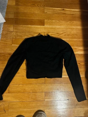 Svart croppad långärmad tröja - En svart croppad tröja med lång ärm och hög hals. Tröjan har en enkel och stilren design som passar perfekt till jeans eller kjol. Materialet ser ut att vara mjukt och stretchigt, vilket ger en bekväm passform.