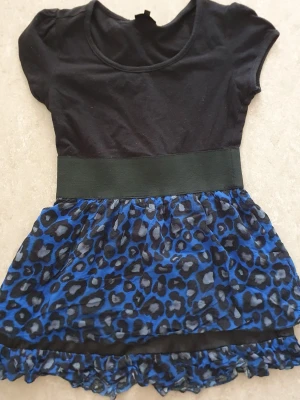 Klänning - Klänning från KappAhl med svart överdel och korta ärmar. Kjoldelen är blå och svart med leopardmönster och har volangkant nertill. Bred midjeresår för snygg passform. Perfekt för dig som gillar djurmönster och färg.