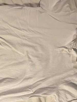 Vit Pique från Bruun & Stengade - Klassisk vit henley från Bruun & Stengade med rund halsringning och knappar framtill. Tillverkad i mjuk bomull som känns skön mot huden. Perfekt för en clean och enkel stil.