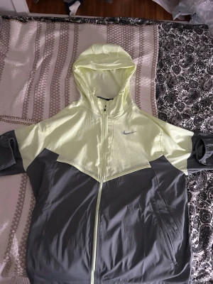 Nike Miller kofta   - Snygg vindjacka från Nike i tvåfärgad design med ljusgul ovandel och grå nederdel. Jackan har huva, hel dragkedja framtill och två sidofickor. perfekt för blåsiga dagar. Nike-logga på bröstet för en sportig look. Folk med både m och s kan använda den. Köpte den för 1250. Knappt använd. 