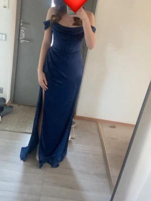 Marinblå balklänning med slits - Elegant marinblå balklänning i satinliknande material med offshoulder-design och hög slits på ena sidan. 