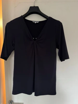 Marinblå elegant tröja med v-ringning  - Marinblå topp med v-ringning och snygg rynkning framtill som hålls ihop av två små pärlor. Tröjan är i mjukt, stretchigt material som sitter bekvämt :) 