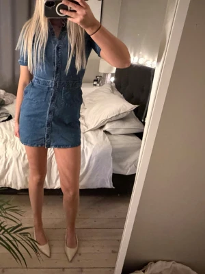 Kort jeansklänning med fickor - Snygg kort jeansklänning i blå denim med korta ärmar från Zara. Klänningen har en markerad midja och knappar längs framsidan.