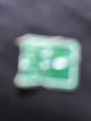 Grön rektangulär pryl - En grön, rektangulär sak med ljusare kanter. Formen är tydlig men detaljer är svåra att urskilja. Kan vara tillverkad av plast eller liknande material.