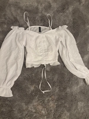 Vit offshoulder topp från H&M  - Supersöt vit offshoulder topp från H&M Divided med långa puffärmar, smala axelband och snörning framtill. Toppen har en croppad passform och volangkant vid ärmslut och axlar. Perfekt för en trendig och luftig look. Tunt material och bra kvalitet perfekt för sommaren.