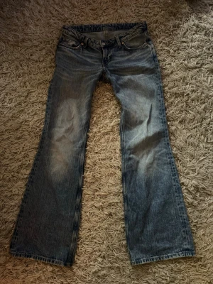 Weekday  bootcut blå jeans - Säljer ett par klassiska blå Levi's jeans med bootcut passform och slitningar på framsidan. Jeansen har fem fickor, gylf med dragkedja och knapp samt en läderpatch bak i midjan. Perfekta för en avslappnad och tidlös stil. Lågmidjade, finns en liten skada men inte hål eller något man tänker på ( se sista bild )