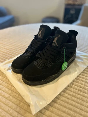 Svarta Air Jordan 4 Retro sneakers - HELT OANVÄND.Säljer ett par helsvarta Air Jordan 4 Retro sneakers med meshdetaljer och Jumpman-logga på plösen. Skorna har en chunky sula, svarta skosnören och coola plastdetaljer vid snörningen. Perfekta för dig som gillar streetwear och klassisk basketstil.