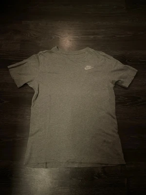 Grå Nike t-shirt i bomull - En stilren grå t-shirt från Nike med klassisk logga på bröstet. T-shirten har rund halsringning och korta ärmar, perfekt för en avslappnad look. Tillverkad i mjuk bomull för skön komfort.