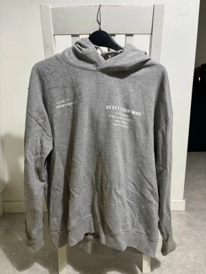 Hoodie - En grå hoodie med litet vitt tryck på bröstet. 