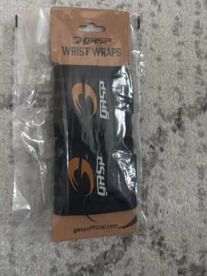 GASP Wrist Wraps - Säljer ett par helt nya svarta handledslindor från GASP med guldigt logotryck och vita ränder. Perfekta för styrketräning och gym. Elastiskt material med tumögla för enkel användning och extra stöd vid tunga lyft.