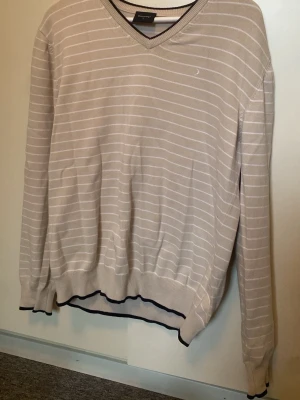 Beige stickad tröja med ränder - Snygg beige stickad tröja från Boomerang med tunna vita horisontella ränder. Tröjan har V-ringning, långa ärmar och ribbade muddar med svart kant. Älskar detta stilrena plagg men tyvärr för stor för mig💔 En liten fläck på framsidan som syns på andra bilden