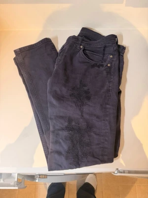 Mörkblå jeans med patchade detaljer - Säljer ett par mörkblå jeans med unika patchade detaljer på framsidan. 188cm, 69kg passar perfekt om man är ute efter baggy jeans,! Jeansen har klassisk femficksdesign, raka ben och silverfärgade nitar. Materialet är denim med en mjuk känsla. Perfekta för dig som gillar en personlig och avslappnad stil.