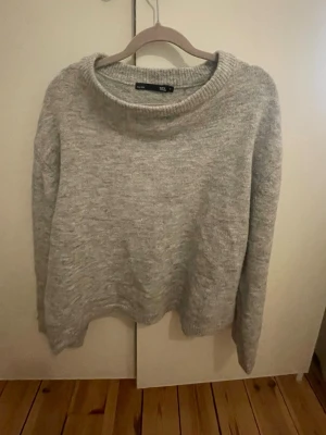 Ljusgrå stickad tröja lager 157 - Mysig ljusgrå stickad tröja från lager157 med rund halsringning och långa ärmar. Tröjan har en enkel och avslappnad passform, perfekt för lager på lager. Materialet är stickat av mjukt garn.