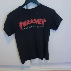 Svart t-shirt med japanskt tryck - Cool svart t-shirt med rött och vitt japanskt tryck på bröstet. Klassisk rund hals och korta ärmar. Perfekt för dig som gillar streetwear och grafiska prints. Materialet känns mjukt och bekvämt, troligen bomull.