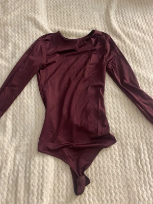 Vinröd body från Amisu - Snygg vinröd body från Amisu med långa ärmar och rund halsringning. Tillverkad i ett mjukt, stretchigt material som sitter tight mot kroppen. Praktisk knäppning i grenen för enkel på- och avtagning. Perfekt att styla med jeans eller kjol.