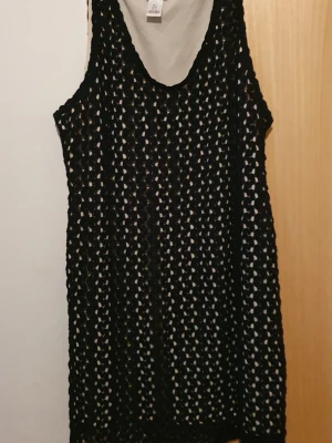 Klänning - Säljer en svart virkad kortklänning från Motherhood Maternity. Klänningen är ärmlös och har ett grovmaskigt mönster samt en vit snörning i midjan som detalj. Perfekt för lager på lager och ger en cool, avslappnad vibe.