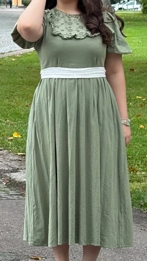 Grön blommig klänning  - Söt grön klänning från med broderade blommor och volangdetaljer vid bröstet. Klänningen har korta volang ärmar, rund halsringning. Perfekt för sommarens alla tillfällen. Klänningen har inga skador och använd bara en gång.