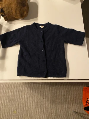 Mörkblå kofta från Gina Tricot - Mörkblå kofta från Gina Tricot med korta ärmar och rund halsringning. Koftan har knappar framtill och är stickad i ett mjukt material. Helt ny och bara använd en gång.