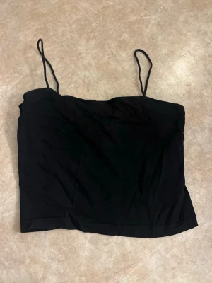 Svart croppad linnetopp - Säljer en enkel och stilren svart croppad linnetopp med tunna axelband. Perfekt att matcha med höga jeans eller kjol. Materialet känns mjukt och lätt, vilket gör den skön att bära under varma dagar.